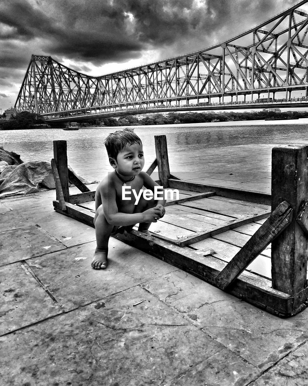 Shirtless boy with bridge over lake in background