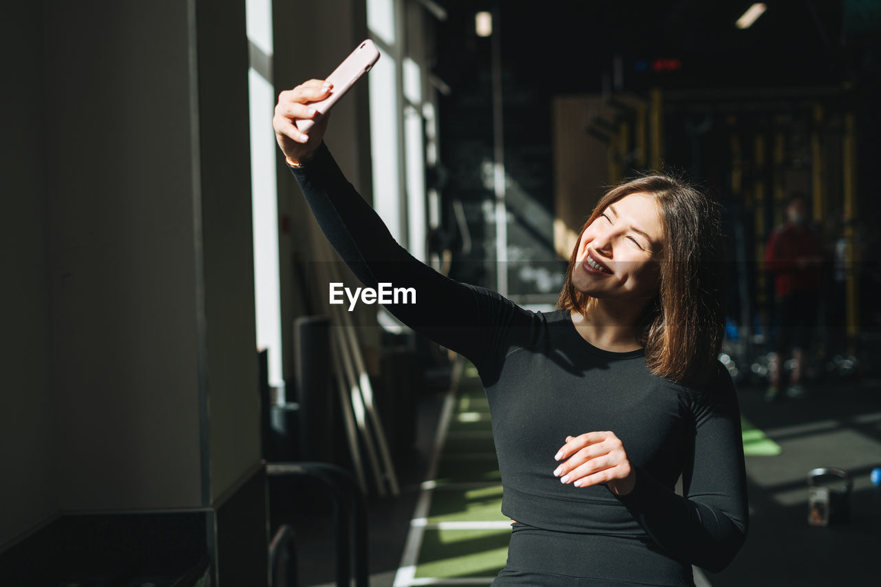 Portrait of resting young brunette woman in sport active wear taking selfie in fitness club