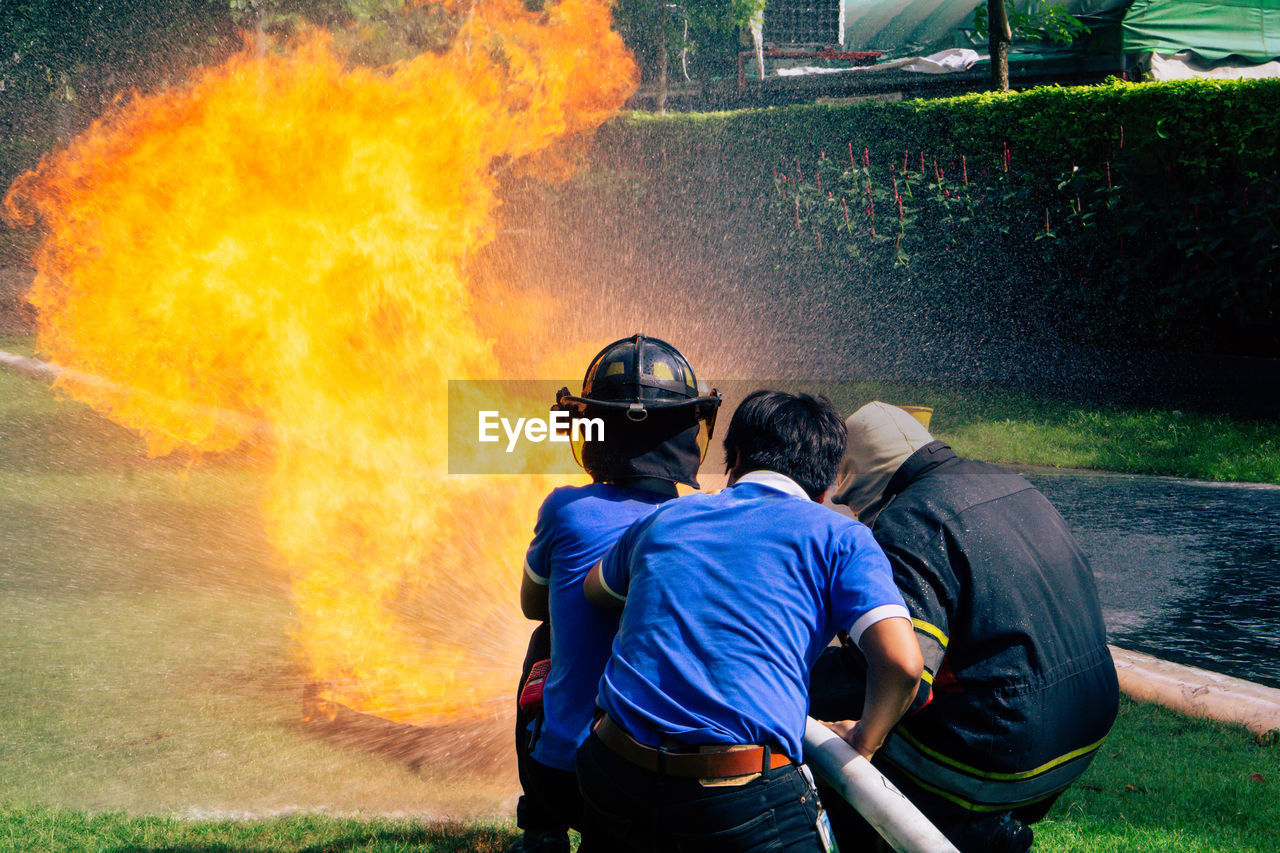 REAR VIEW OF TWO MEN WITH FIRE ON THE BACKGROUND