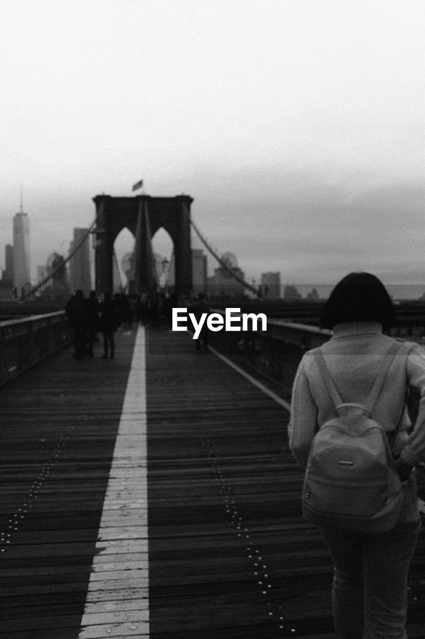 Rear view of woman standing on suspension bridge against sky