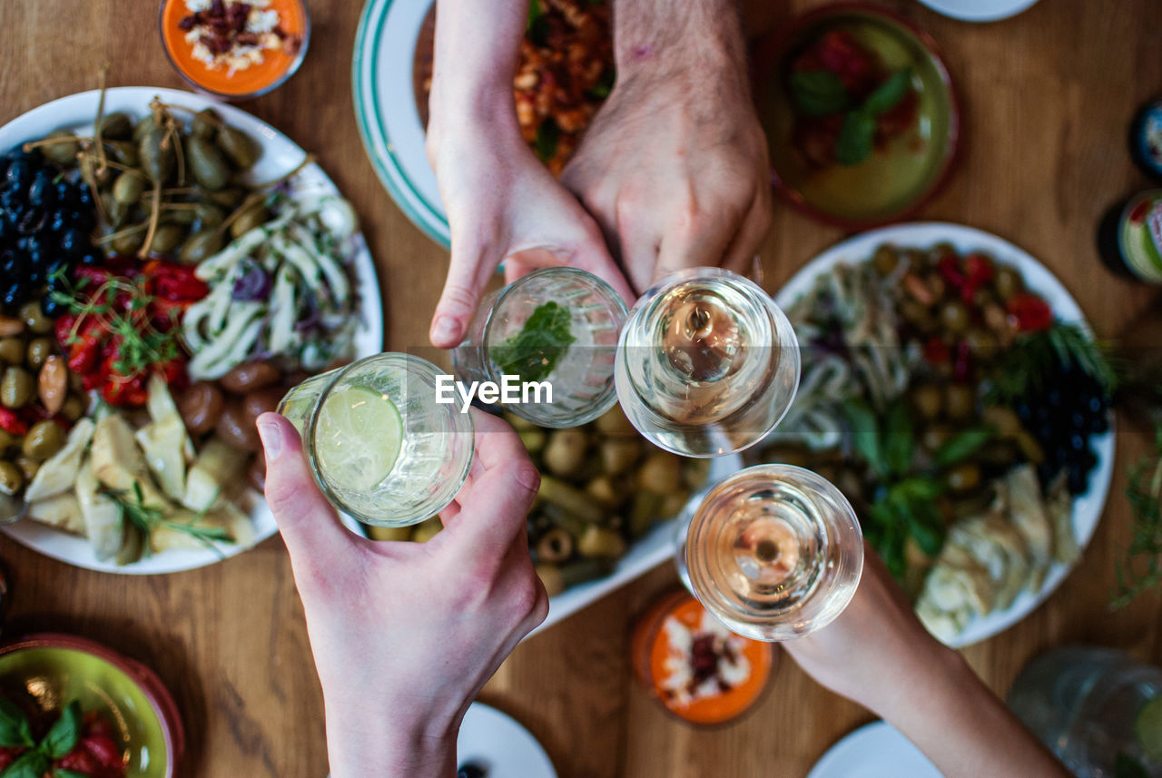 Cropped image of friends toasting drinks over food on table