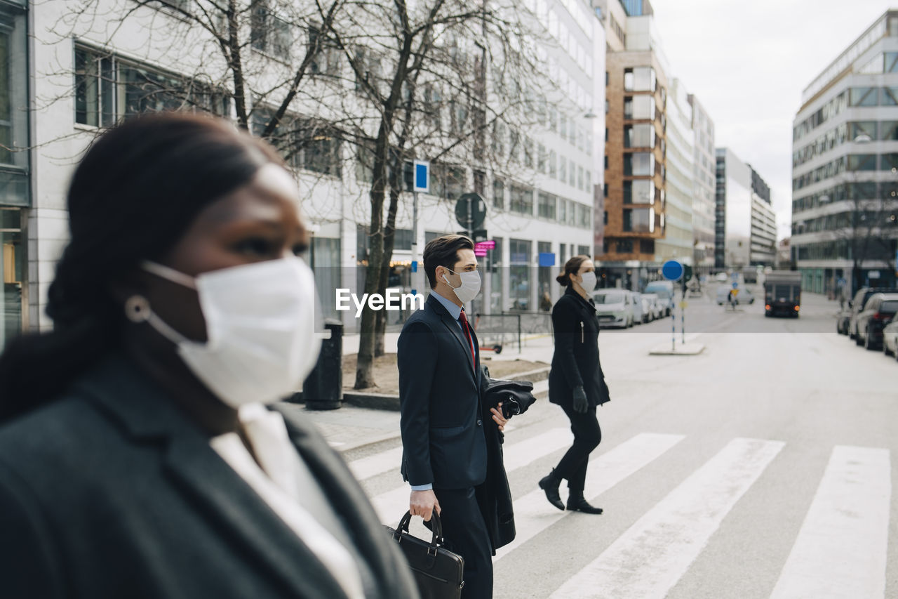 Female and male colleagues crossing street in city during pandemic