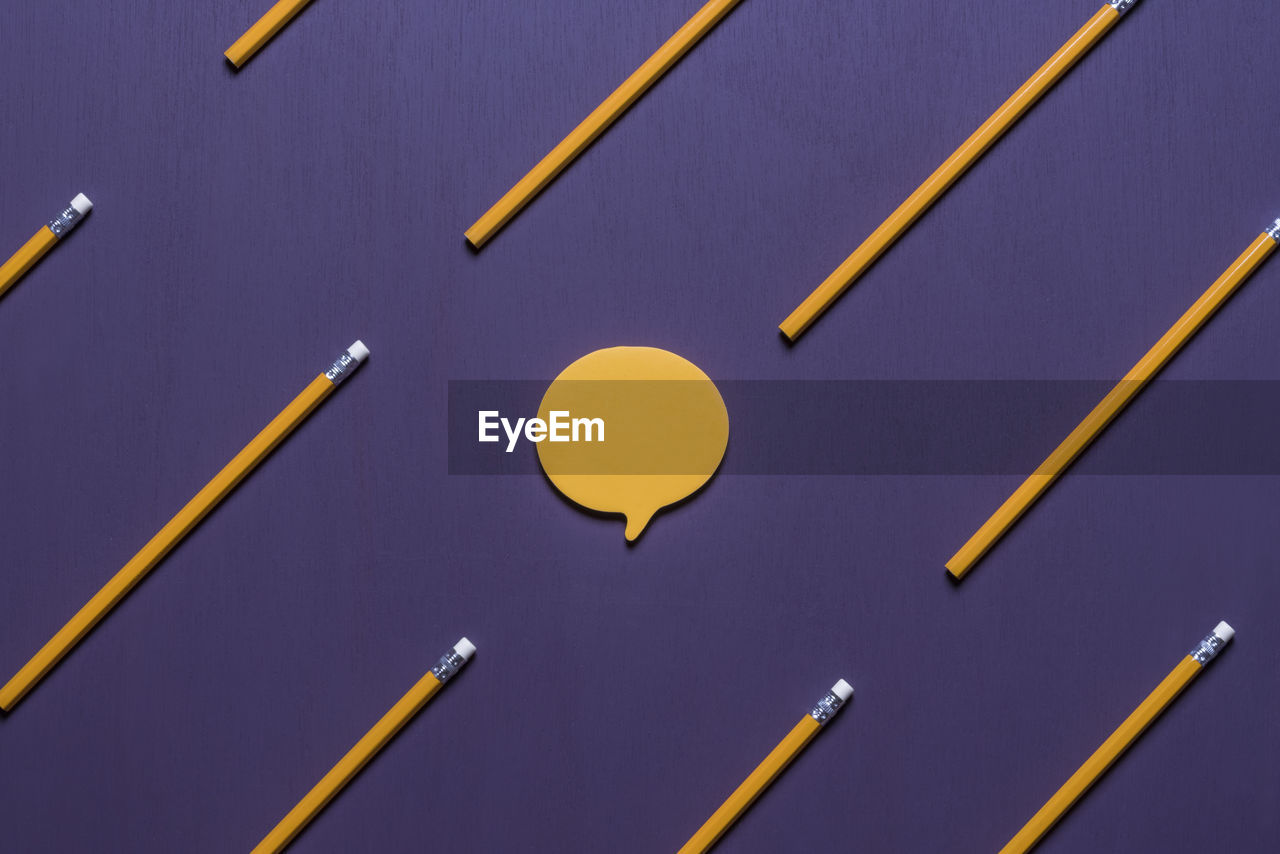 Close-up of yellow pencils and speech bubbles on purple table