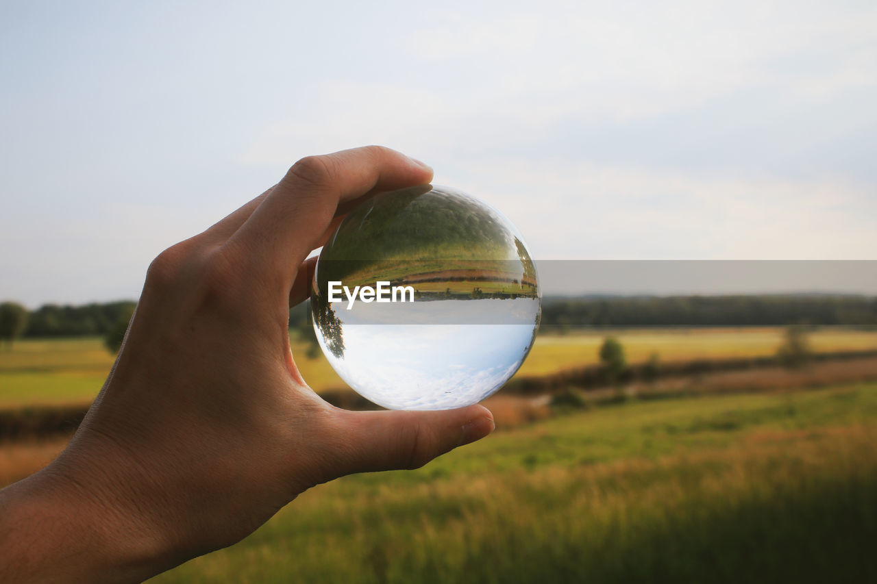 Cropped hand holding crystal ball on landscape