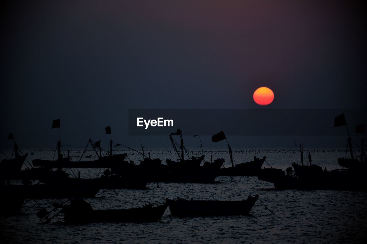 Silhouette boats in calm sea at sunset