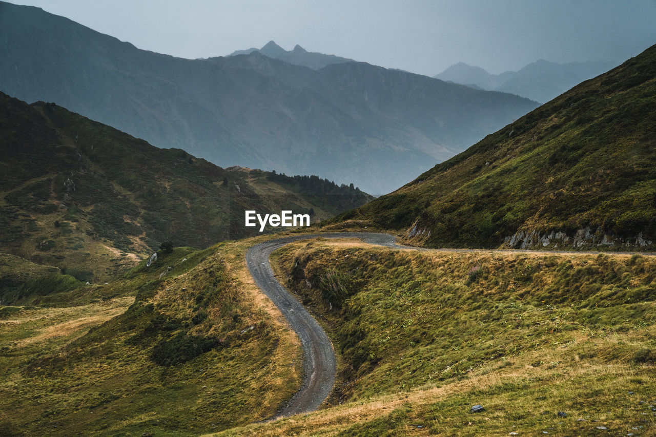 Picturesque landscape of empty route surrounded with dry and green grass in mountainous terrain of aran valley in spain under gray cloudy sky