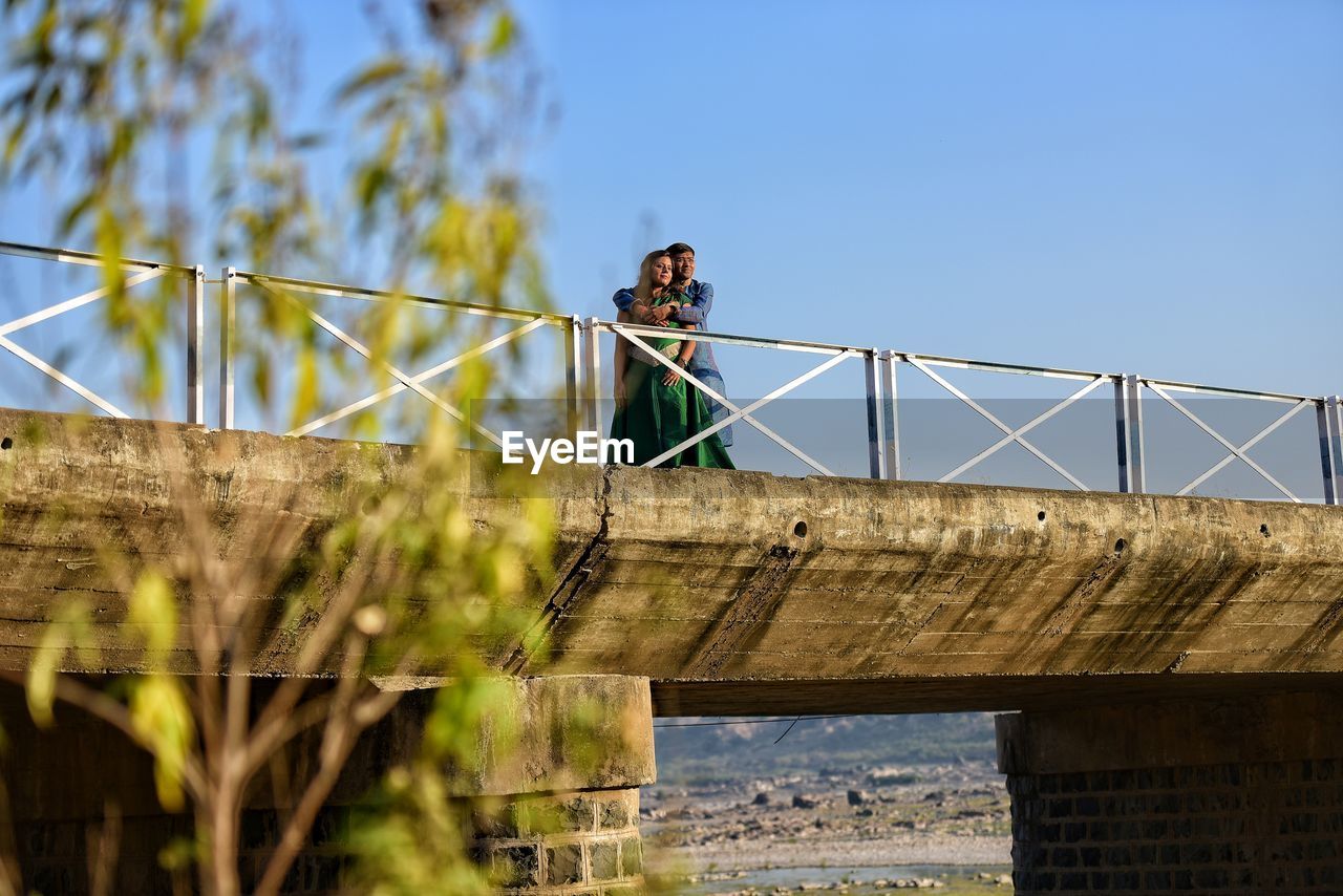 Low angle view of young couple on bridge against sky