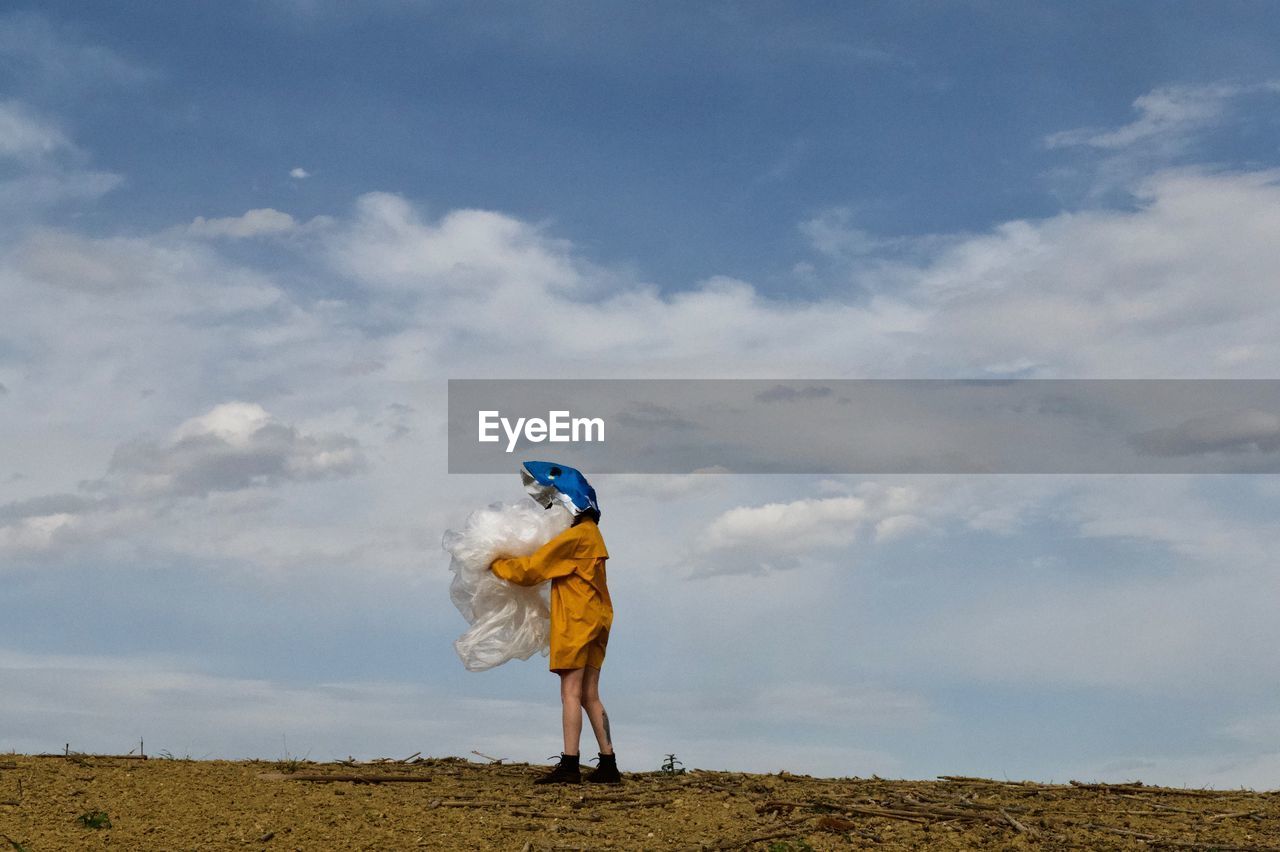 Woman wearing mask holding fabric against sky on land