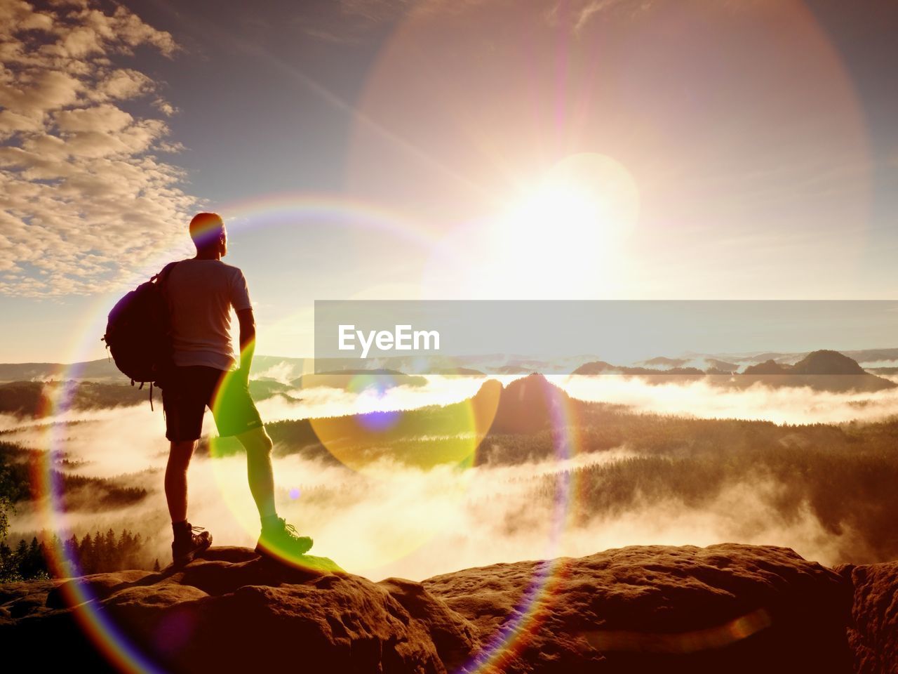 Flare. thinking hiker in black on rocky peak. ginger hair man in black pants on cliff. wonderful day