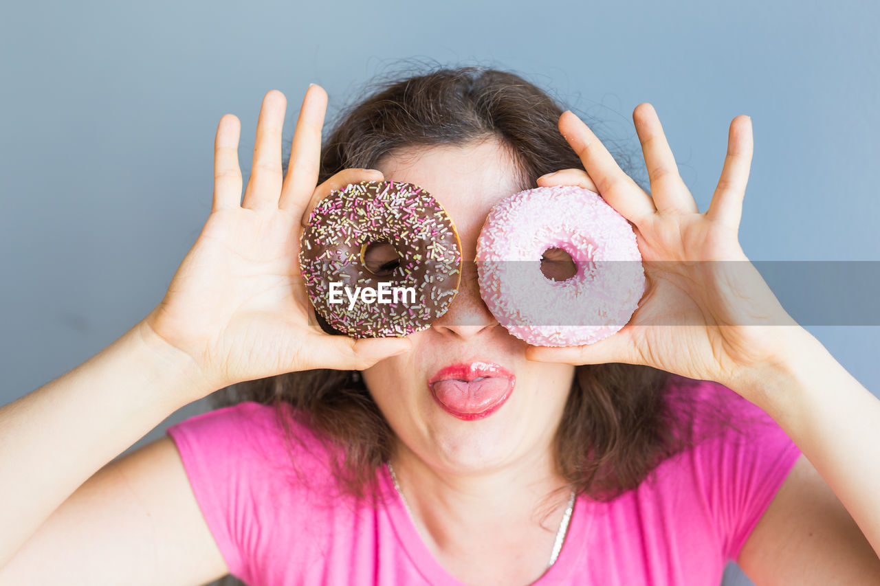 Cheerful woman holding donuts against wall