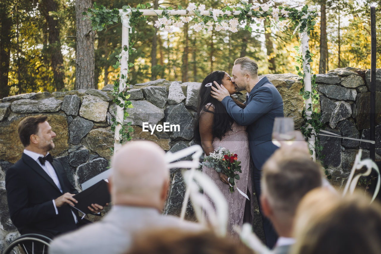 Newlywed couple kissing in front of guests and minister at wedding ceremony