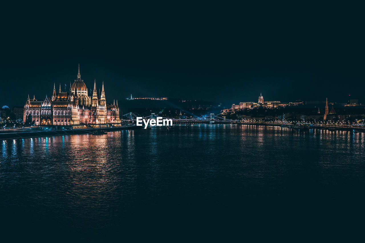 Illuminated hungarian parliament building by river against clear sky at night