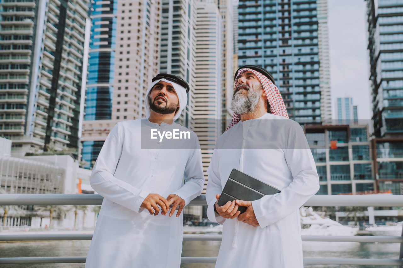 Men wearing dish dash standing against buildings in city