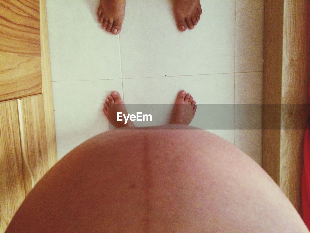 Low section of pregnant woman standing on tiled floor