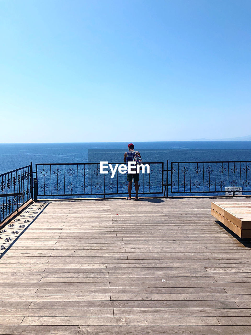 Rear view of man standing by railing against sea and sky