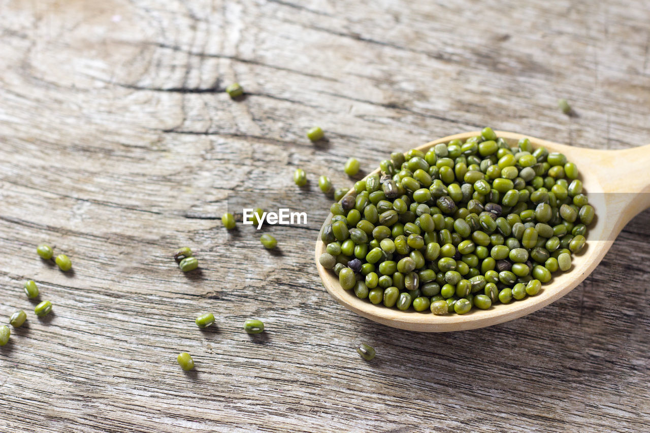 High angle view of scattered mung beans with spoon on wooden table