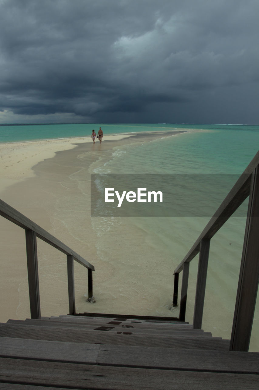 Scenic view of sea with people walking at beach against sky