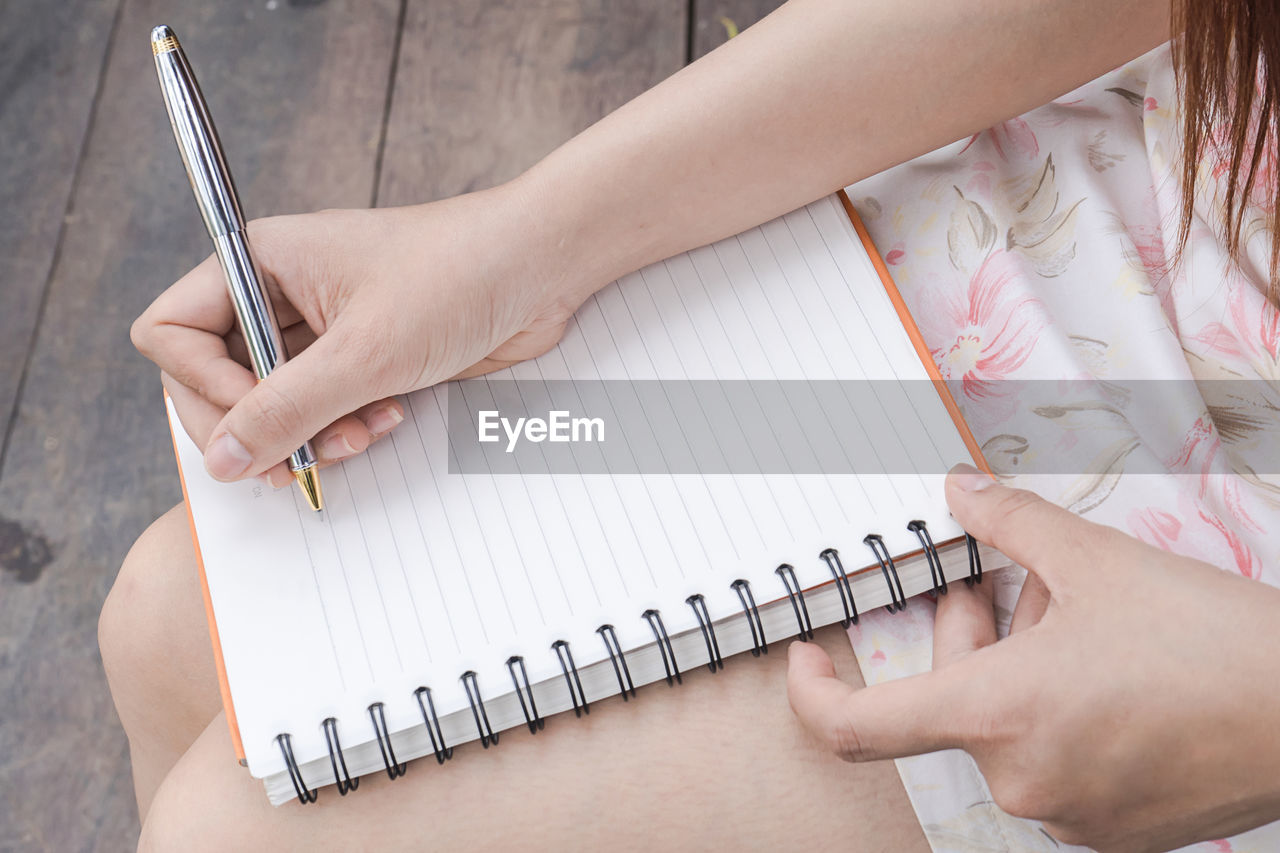 Midsection of woman writing in book at home