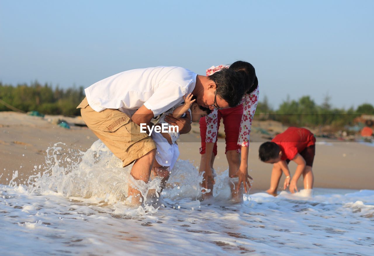 Family enjoying splashing water at beach against sky