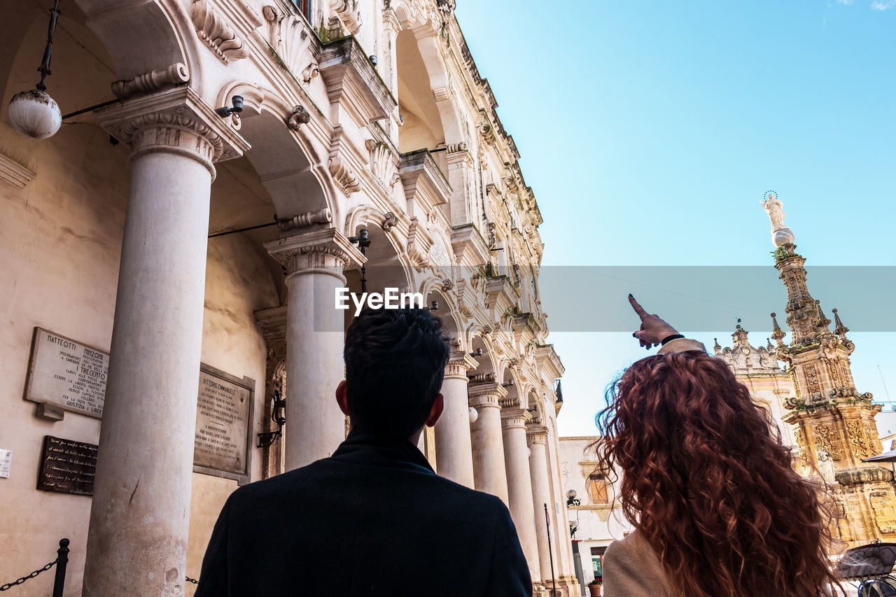 Rear view of people looking at historical building in city