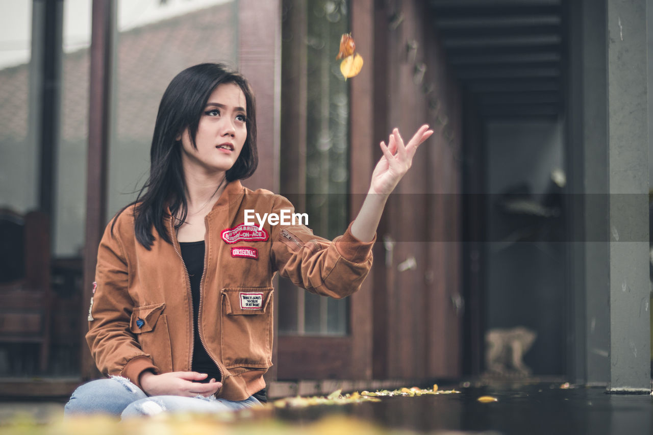 YOUNG WOMAN WITH ARMS RAISED IN FRONT OF BUILDING