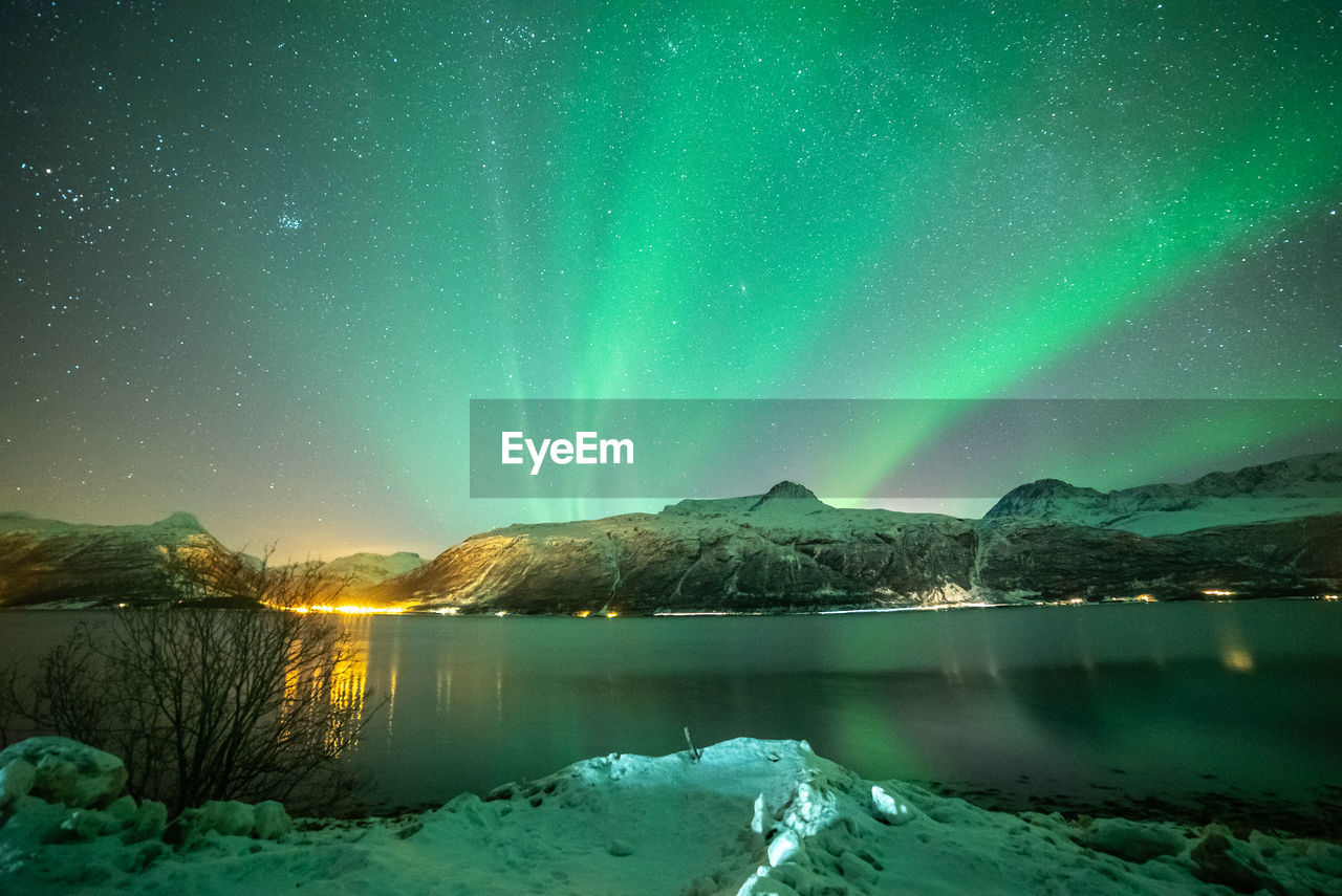 Scenic view of lake by snowcapped mountains against sky at night