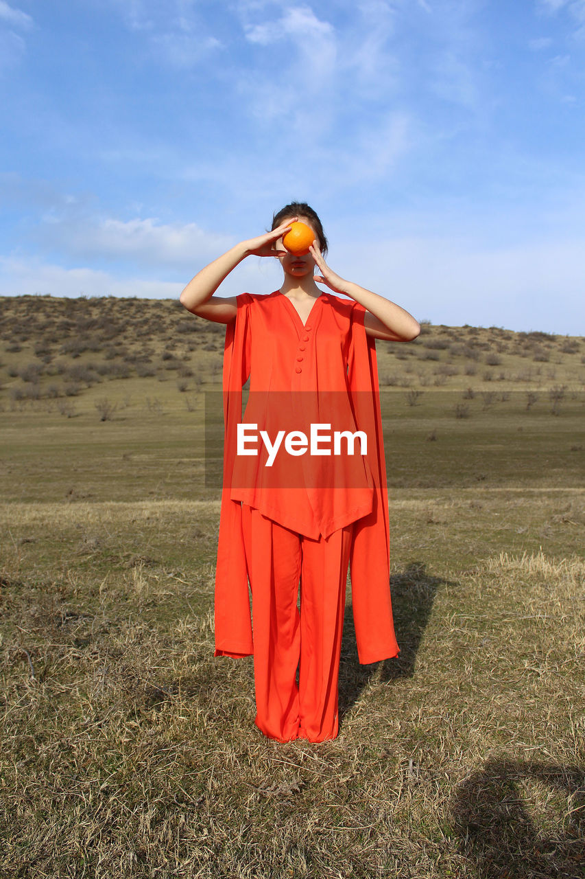 Full length of woman holding fruit while standing on field against sky