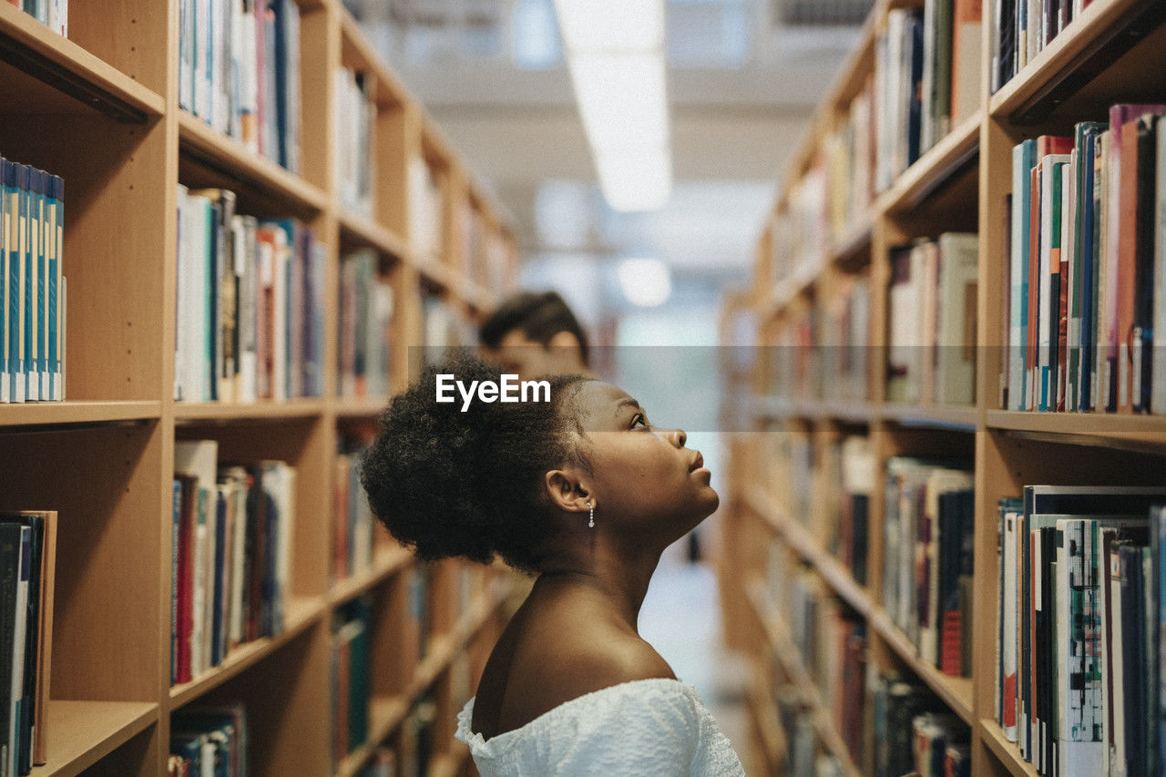 Side view of student searching books on bookshelf in library at university