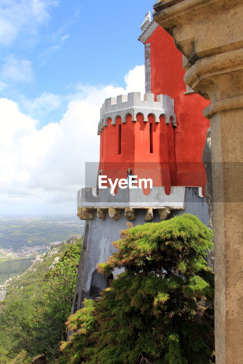 Young woman standing on castle against cloudy sky