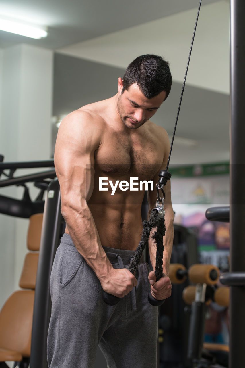 MIDSECTION OF SHIRTLESS MAN HOLDING CAMERA WHILE STANDING IN OFFICE