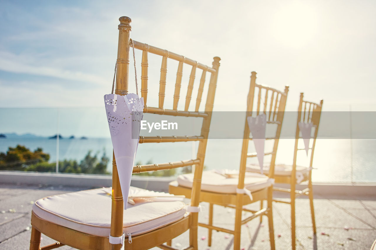 CLOSE-UP OF EMPTY CHAIRS AND TABLE AGAINST SKY