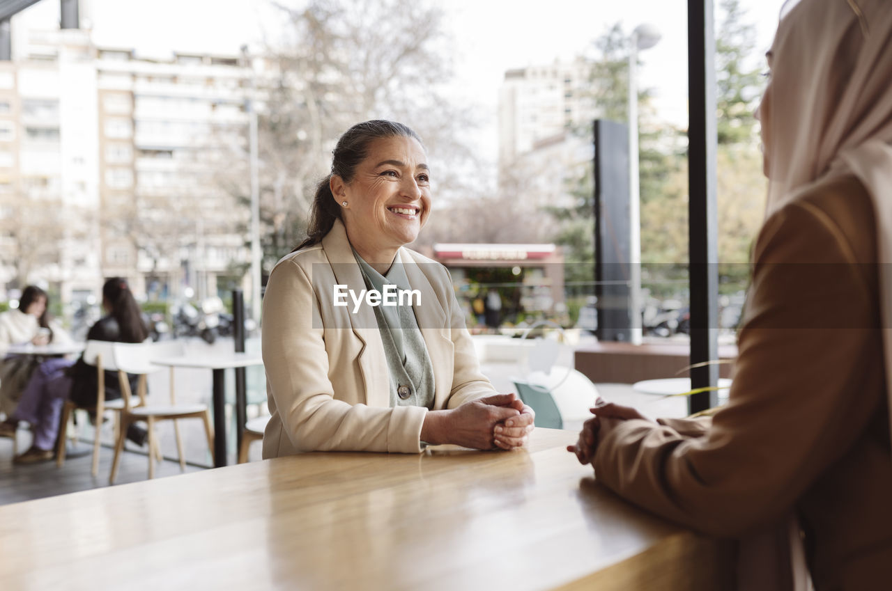 Happy businesswoman talking with colleague sitting at table in coffee shop