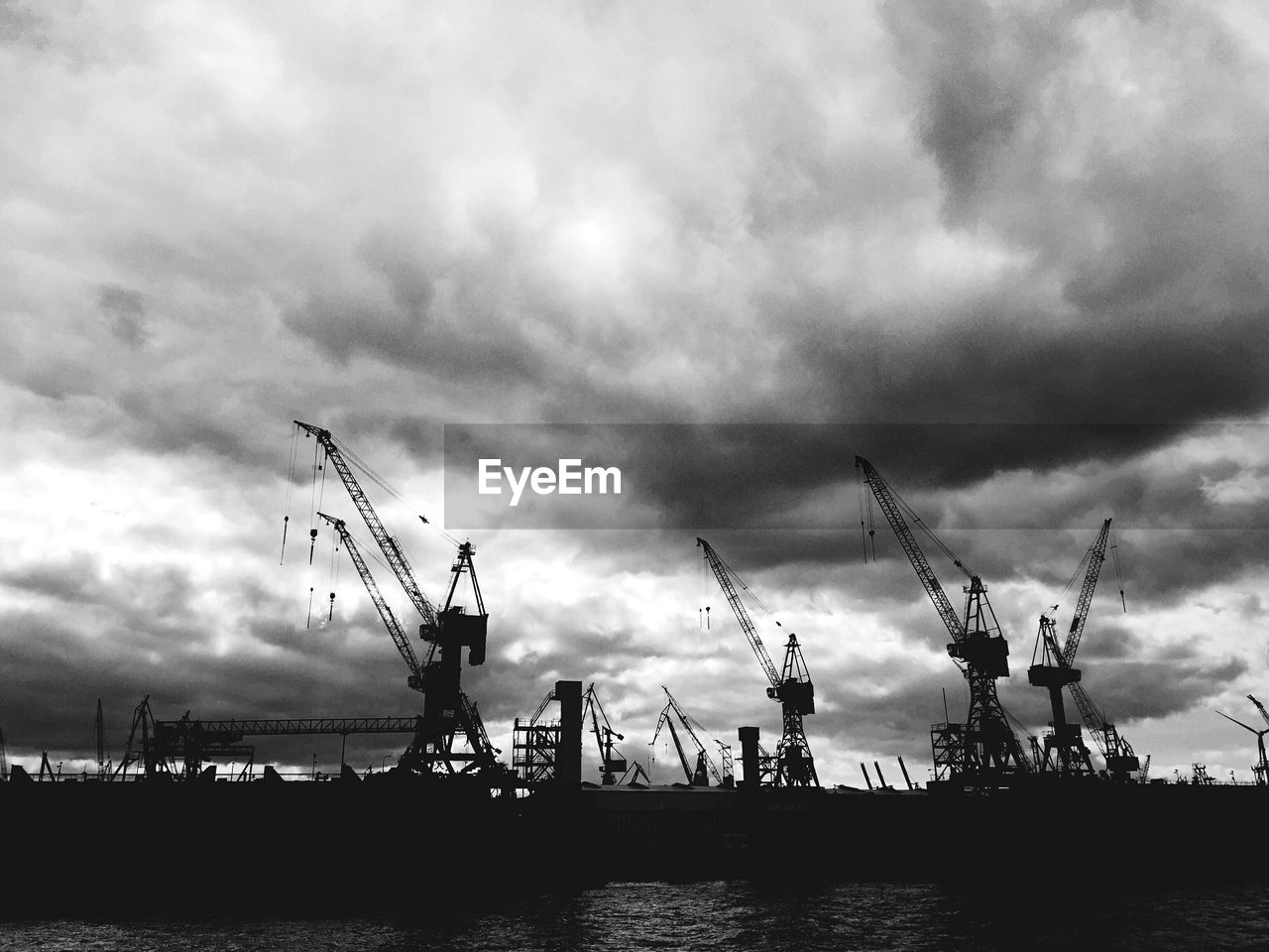 Cranes at commercial dock against cloudy sky