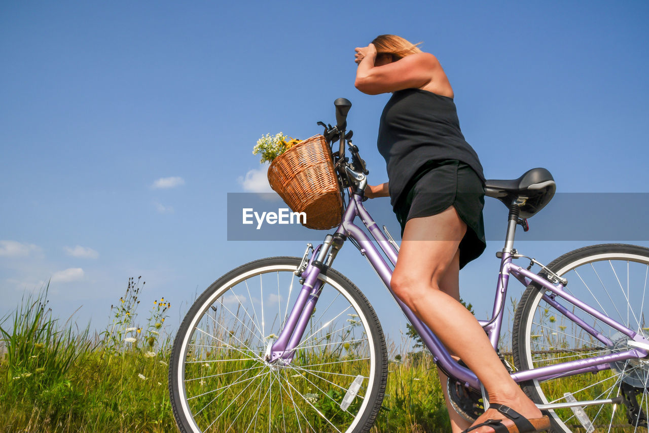 Low angle view of woman riding bicycle on field against blue sky
