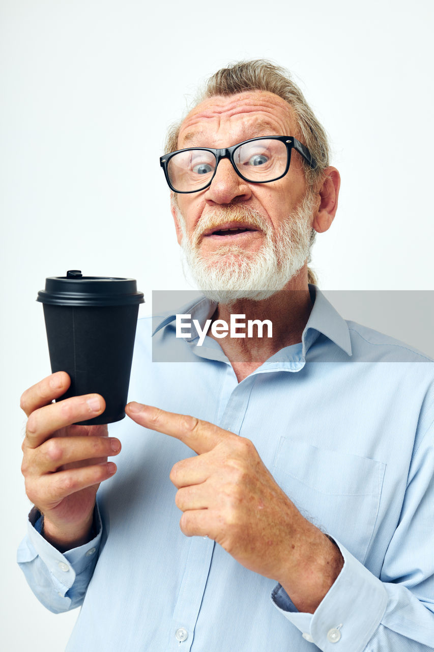 Smiling senior man holding coffee cup against white background