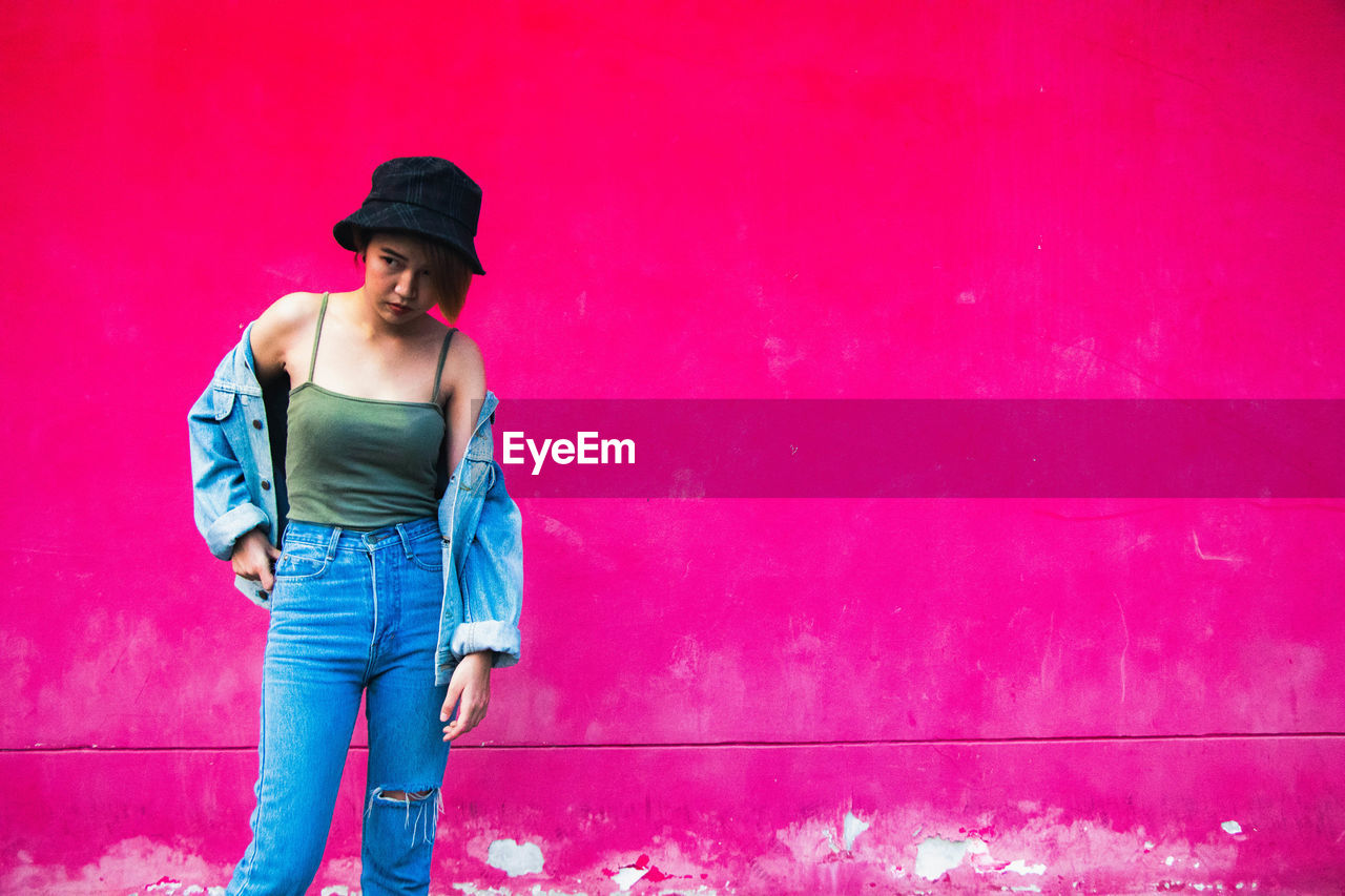 Young woman looking away standing against wall