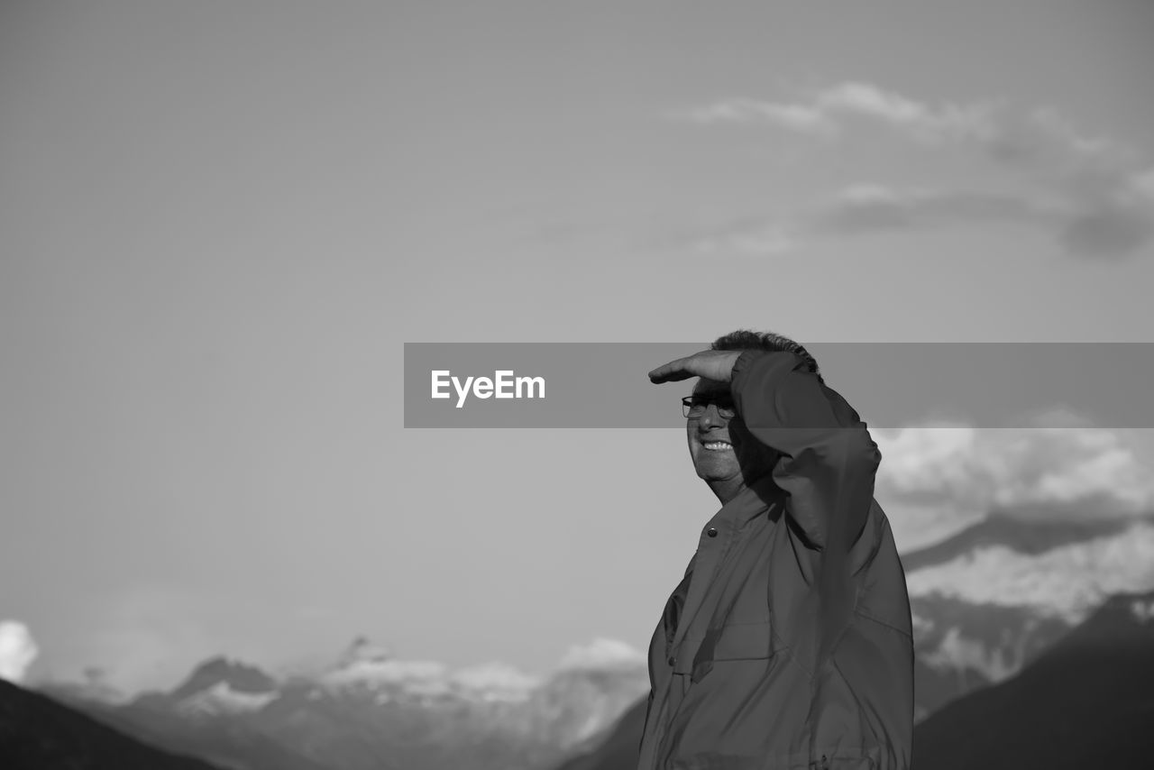 Man shielding eyes while looking away against sky