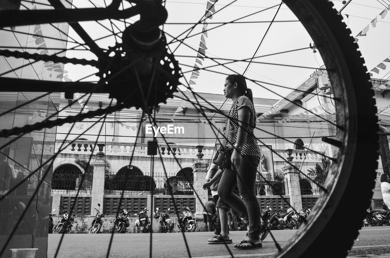 Low angle view of woman walking on street seen through bicycle spokes