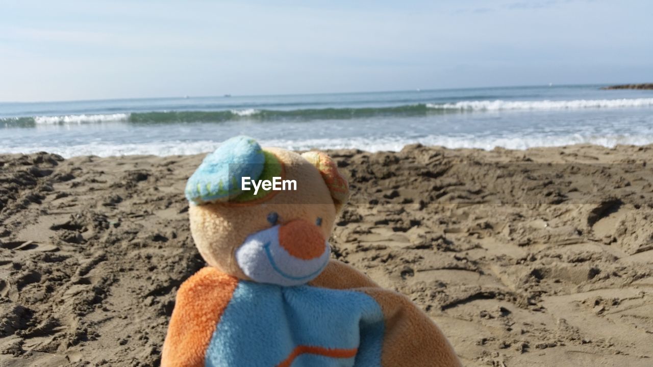CLOSE-UP OF STUFFED TOY ON SAND AT BEACH