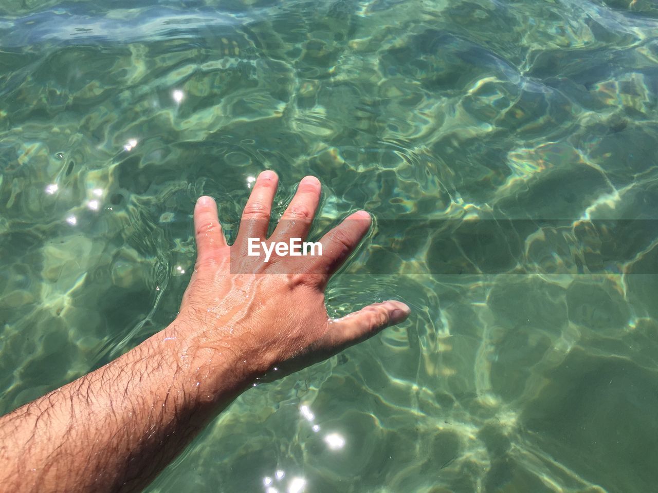 High angle view of hand touching water in sea