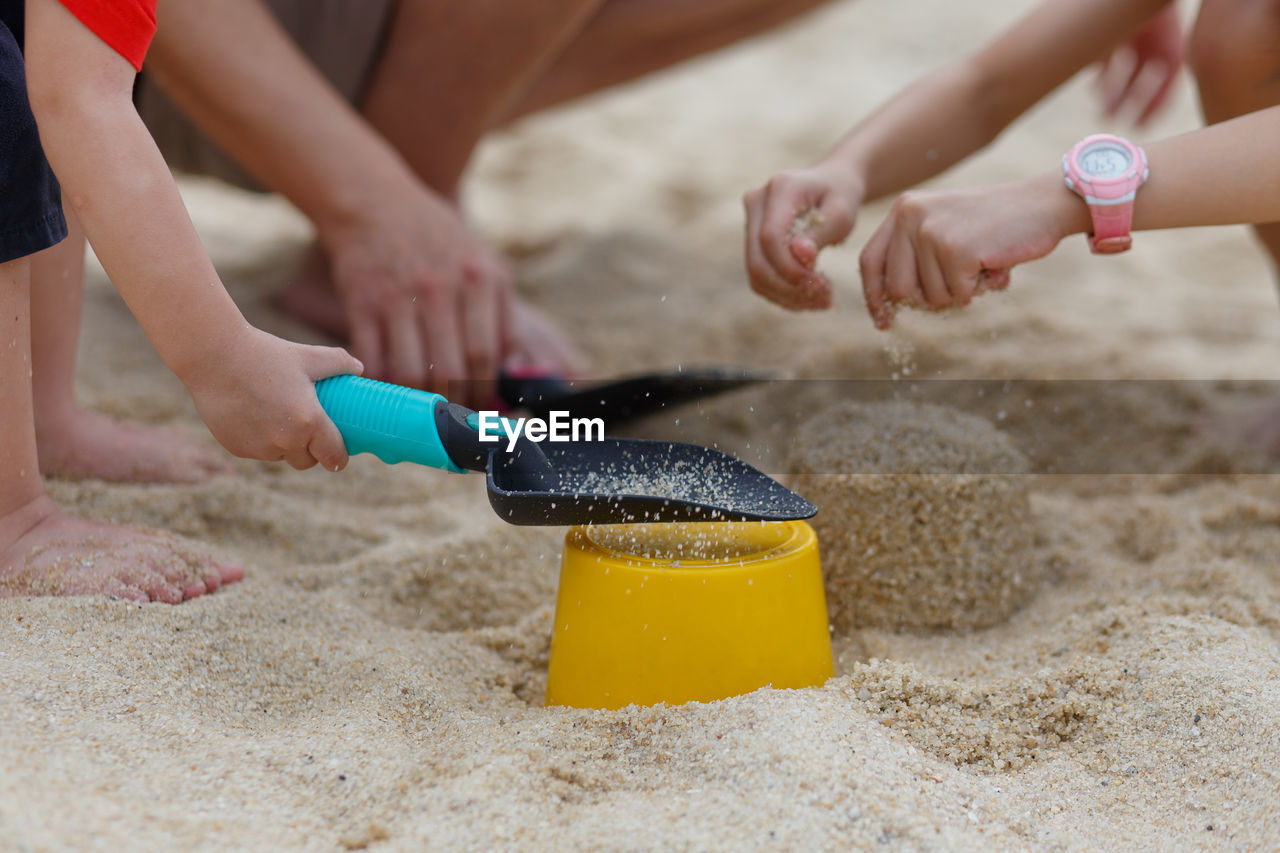 Cropped image of siblings making sand castle at beach