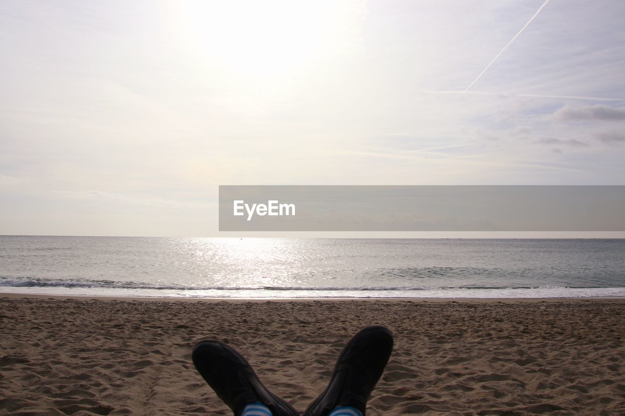 LOW SECTION OF MAN ON BEACH AGAINST SKY