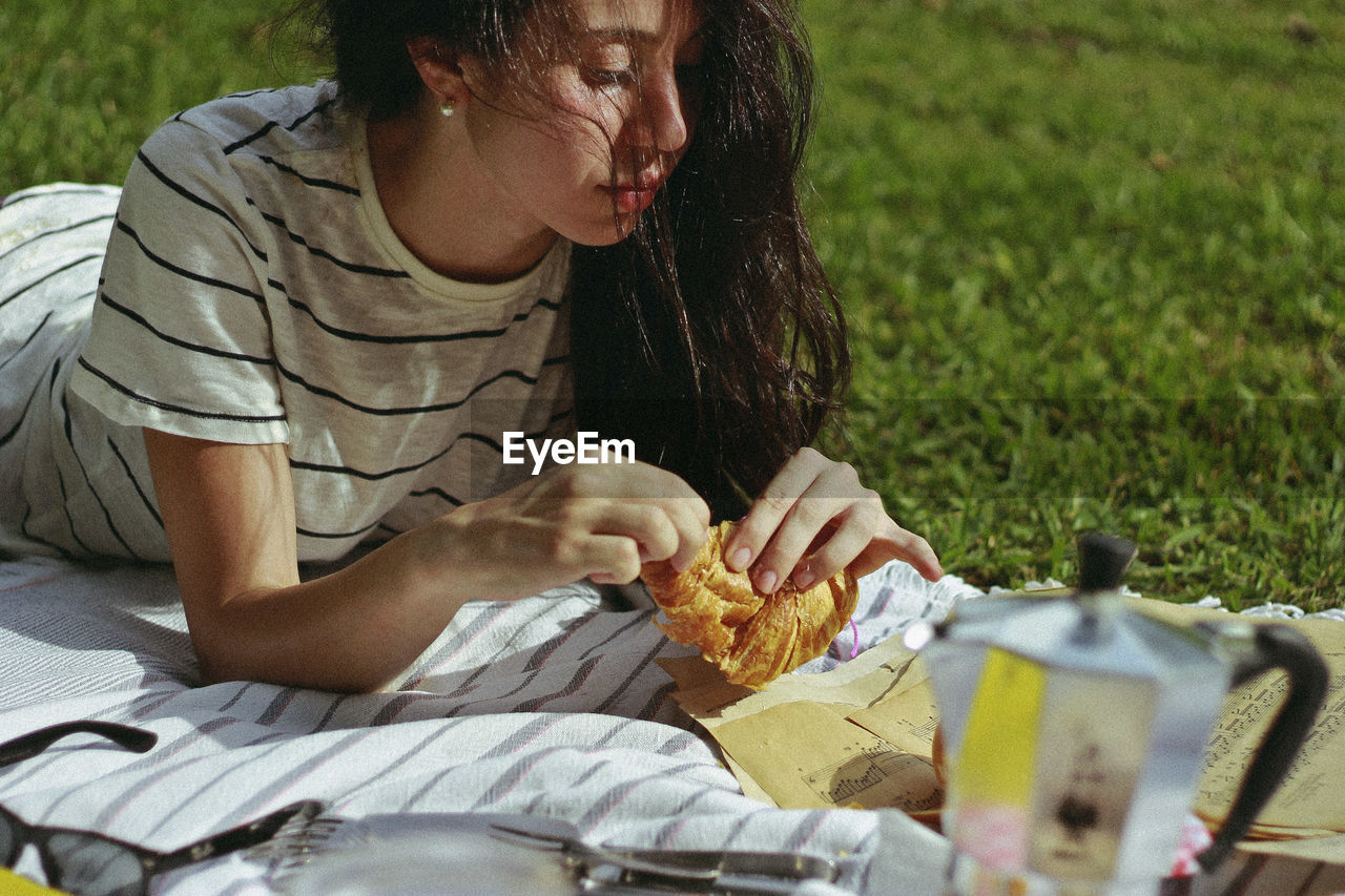 Woman having croissant while reading papers at park