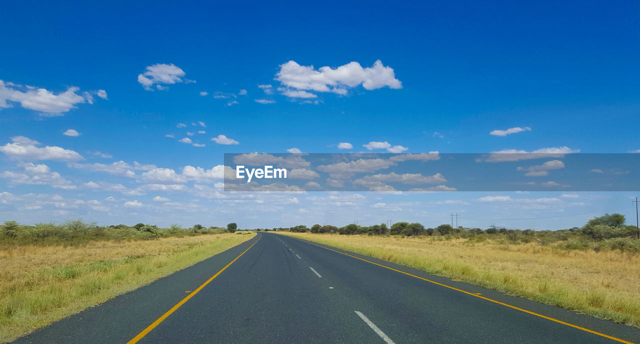 Empty road amidst field against sky