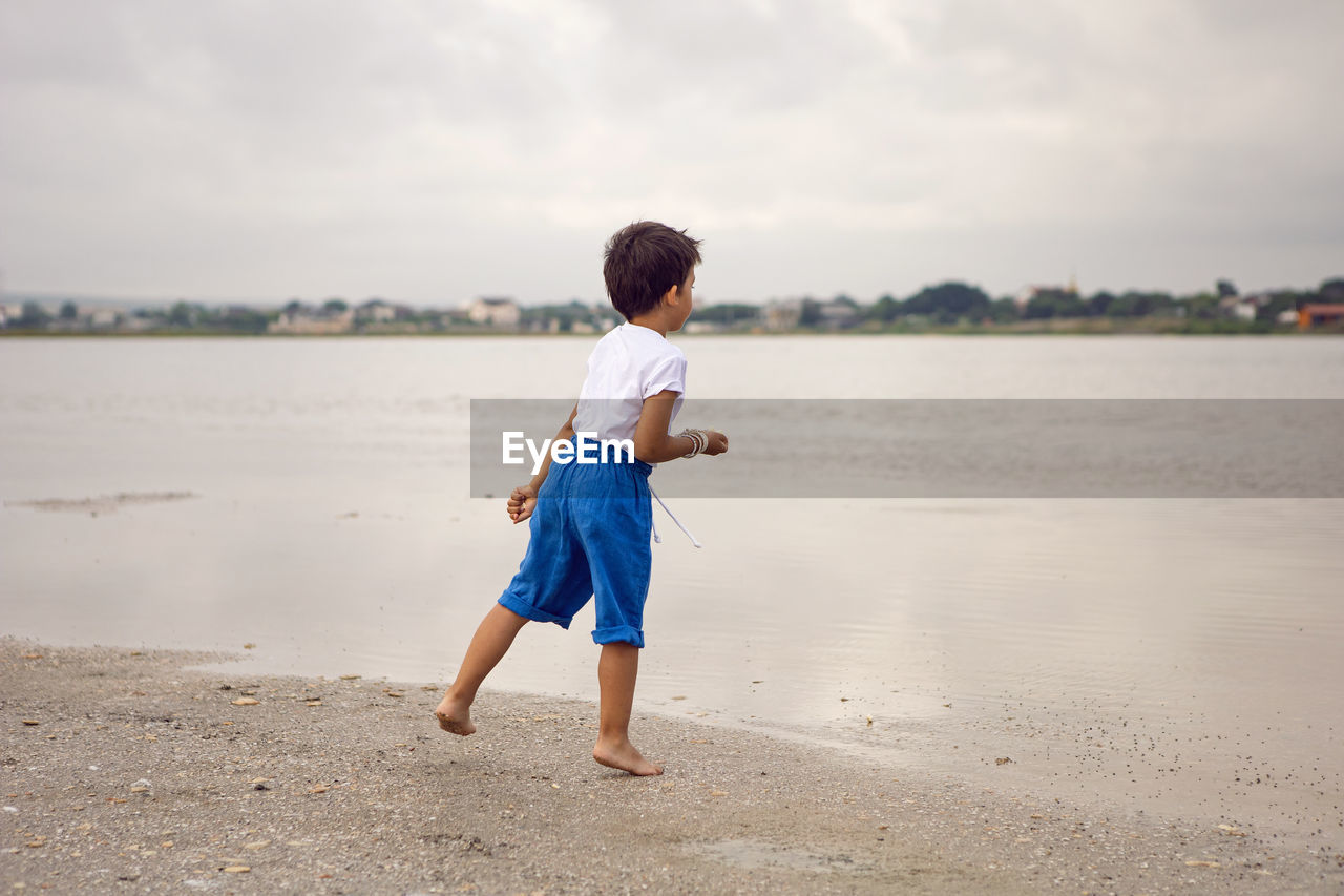 Rear boy child in blue shorts walks by the lake in summer