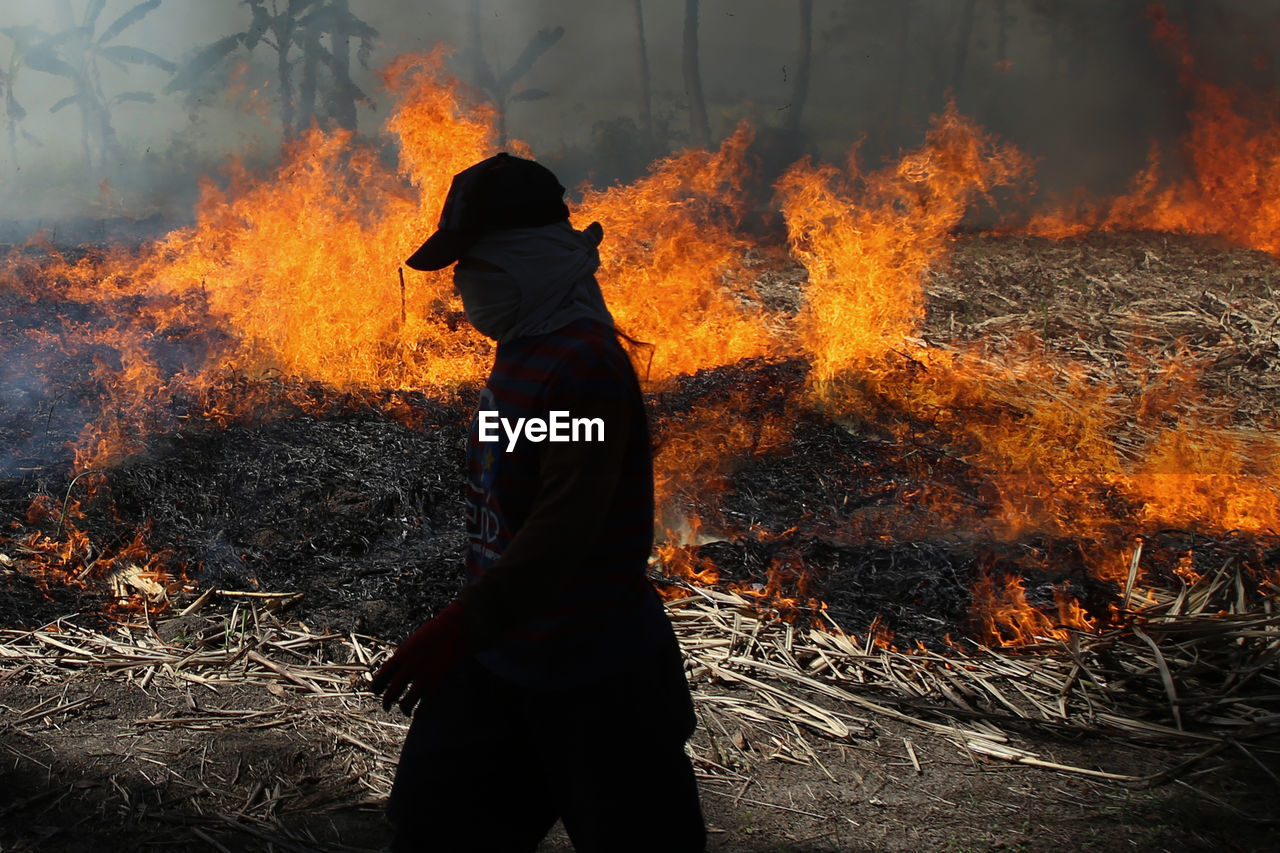 LOW SECTION OF MAN STANDING BY BONFIRE ON FIRE