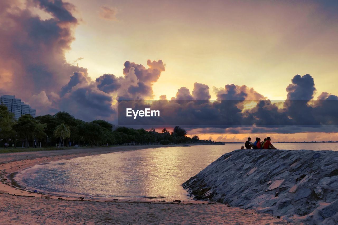 People at beach against sky during sunset