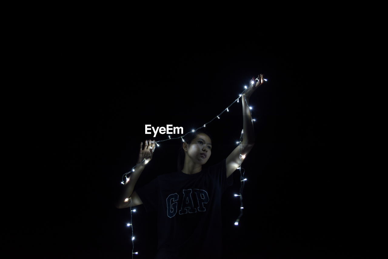 WOMAN STANDING AGAINST ILLUMINATED LIGHTING EQUIPMENT