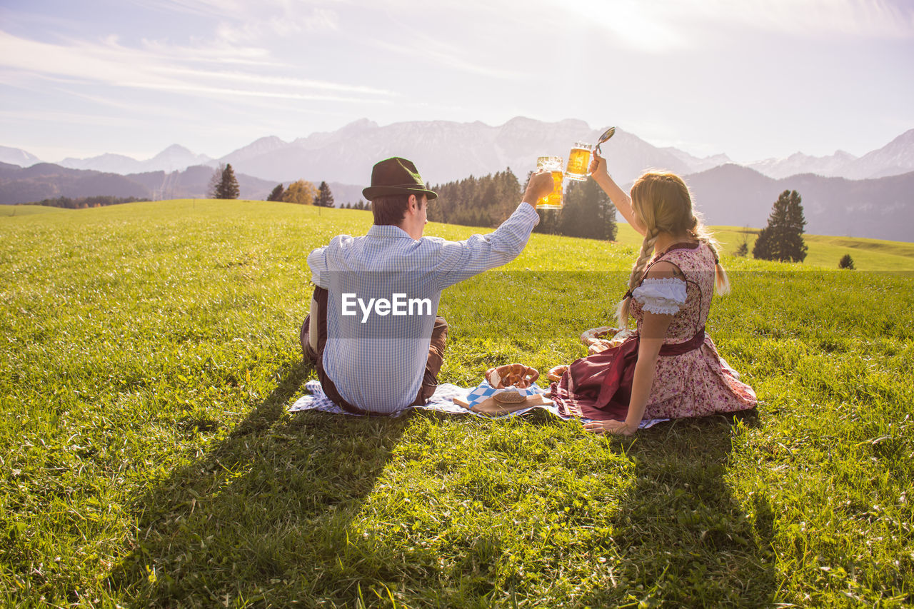 Rear view of couple toasting beer glasses on grassy field