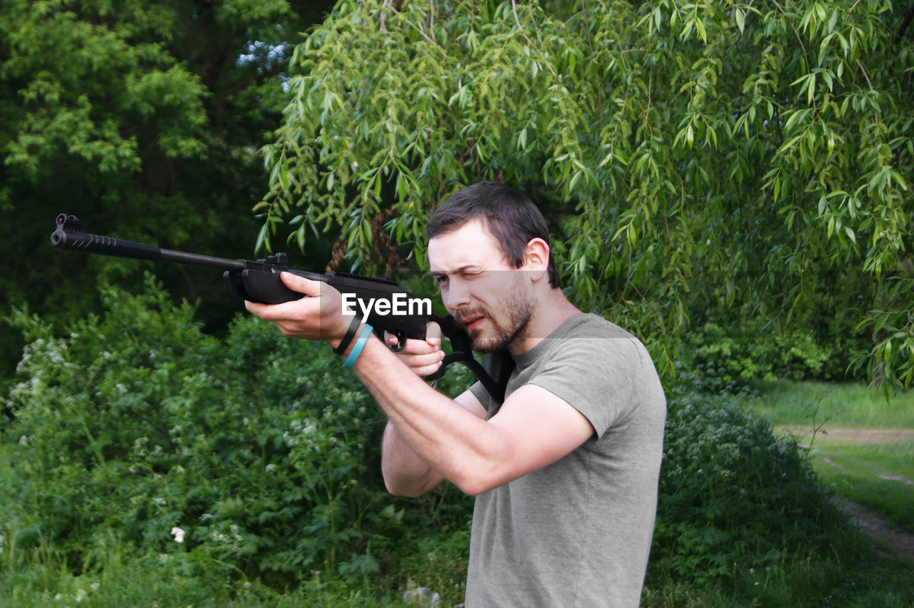 side view of man holding gun against plants